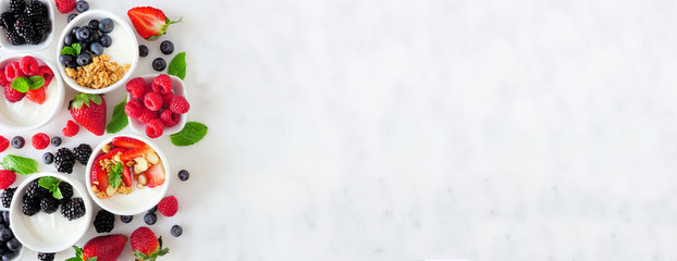 Healthy yogurt bowls with assorted berries and granola. Banner with side border against a white marble background. Copy space.