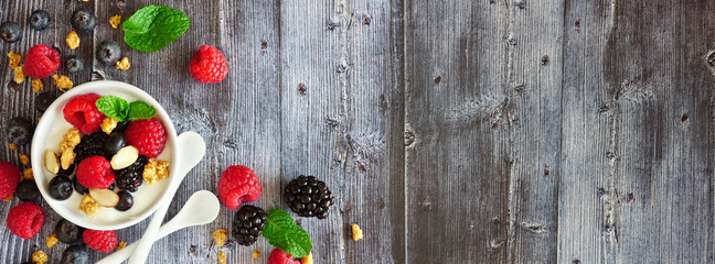 Healthy yogurt with fresh berries and granola. Banner with corner border against a rustic wood background. Copy space.