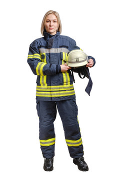 A young brave girl firefighter in a fireproof uniform stands and looks at the camera with a helmet in her hands.