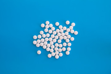Many white round tablets on blue backdrop.