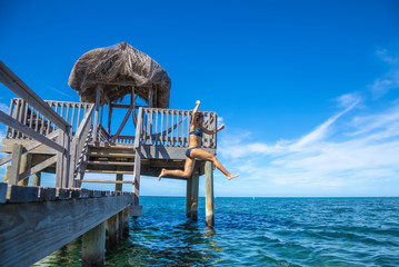 A young tourist girl throwing herself into the Caribbean Sea on Roatan Island from a wooden pier. Honduras