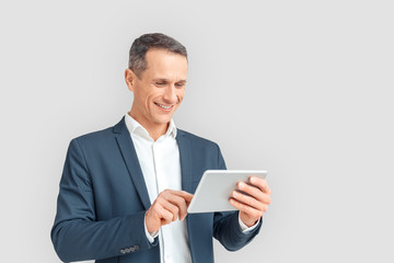 Freestyle. Mature businessman standing isolated on white browsing internet on digital tablet smiling cheerful