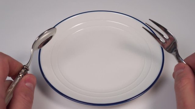 Empty white plate with a blue border on the table in a restaurant. In the hands of a dessert fork and spoon. Table setting. Concept of food and diet restrictions