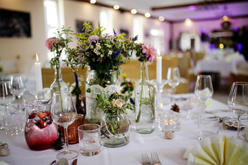 The festive table at the restaurant is decorated with candles and flowers. Wedding reception dinner. Wedding reception dinner. Tables served with candles and rose gold decor stands in restaurant. 
