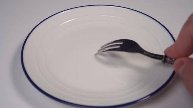 A young man holds a shiny fork on a white plate with a blue border to get a piercing nasty creak. The concept of irritability and nervousness