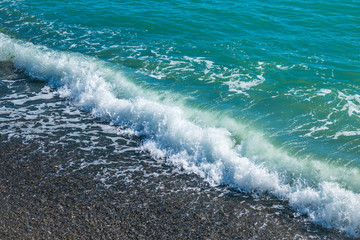 Sea wave with foam on a pebble beach.