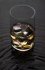 Whiskey Glass with ice on wavy liquid surface.Alcoholic drink with ice cubes on water