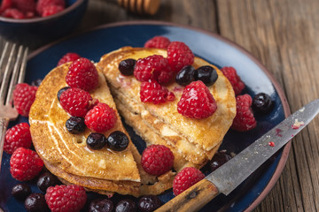 Pancakes with blueberries and raspberries on blue plate on wooden desk.