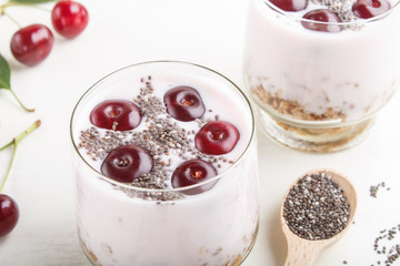 Yoghurt with cherries, chia seeds and granola in glass with wooden spoon on white wooden background. side  view.