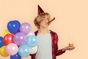 Young man with helium balloons, cupcake and party horn