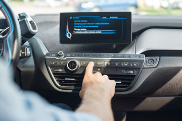 Transportation. Young man traveling by electric car sitting inside pushing button on control panel close-up