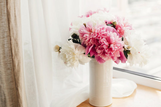 Lovely peony bouquet in sunny light on rustic wooden window sill. Stylish pink and white peonies in vase on wooden background. Hello spring. Happy Mothers day greeting card