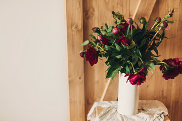 Stylish peony bouquet in white ceramic vase on linen fabric on rustic wooden background. Red and pink peonies rural still life. Hello spring wallpaper. Happy Mothers day. Space text