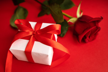 Red rose Gift for valentines day. Top view of present box package decorated into the white paper with red bow-knot. Flat lay on red background. Concept of celebrate. Love and amour.