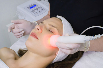 Naklejka premium beautician doing red led light therapy to female customer in beauty salon, facial photo therapy for skin pore cleansing. Anti-aging treatments and photo rejuvenation procedure