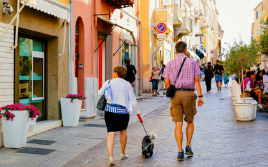 People with pet at Corso Umberto I Street in Old city of Olbia on Sardinia Island in Italy. Tourists and Town architecture on Italian Sardegna. Mixed media.