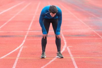 Athlete young man tired, resting on running track .