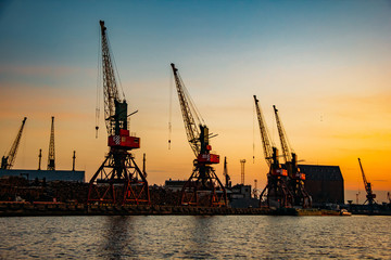 Fototapeta premium Harbor cargo cranes on sunset sky background