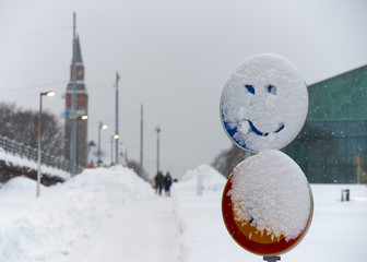 Snowy traffic sign with a smiling face drawn into snow in the center of Helsinki, Finland.