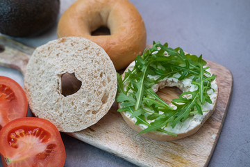 Bagel with rocket, cream cheese, tomato and avocado on a wooden table. Close up view.
