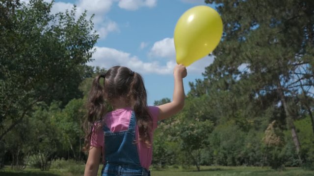 Balloon in the hand. Little girl with a yellow inflatable ball in the fresh air.