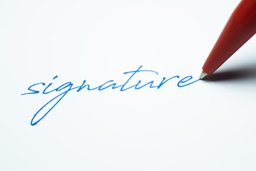 Signature written on paper with a red ballpoint pen
