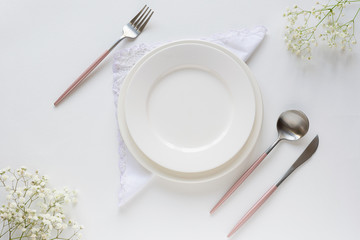 Festive table setting with  empty white plate, pink cutlery, napkin and beautiful flowers. Restaurant menu template. Copy space for your text. Valentine’s day concept.