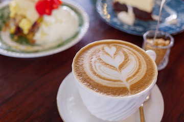 Close up and selected focus view at one cup of cappuccino or latte with flower pattern of latte art in white cup on wooden table. Hipster vibes and vintage tone.