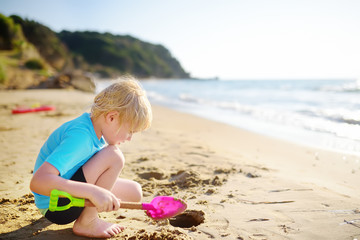 Little boy playing with shovel on sand beach near seashore in Greece