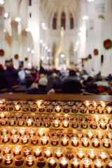 Close-up photo of church candles in transparent chandeliers in Church during catholic religious service.