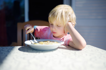 Little boy sitting the table and doesn't want to eat soup. Healthy food.