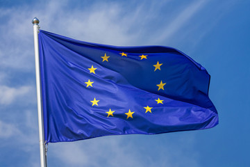 Flag of the European Union waving in the wind on flagpole against the sky with clouds on sunny day, close-up
