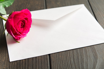 Beautiful pink rose lying on white envelope. Romantic sign with love letter