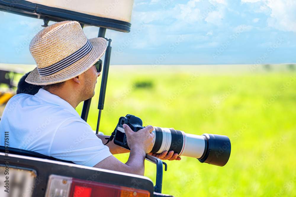 Wall mural The man photographer takes a picture from touristic vehicle on tropical safari.