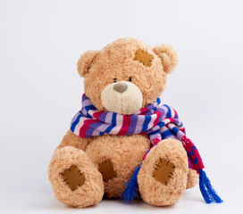 Obraz premium cute brown teddy bear with patches in a colored knitted scarf sitting