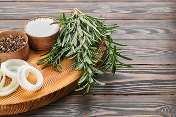 Fresh rosemary, onion and spices on wooden table, closeup