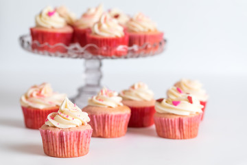 Strawberry cupcakes with cream cheese frosting on a cake stand with more on the table in front for...