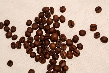 One-tone light background of coarse fabric. Arabica coffee beans are scattered. Caffeine drink.