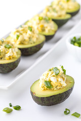 Close up of egg salad in half an avocado garnished with green onion ready for eating.