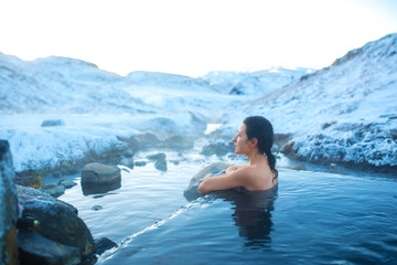 The girl bathes in a hot spring in the open air with a gorgeous view of the snowy mountains. Incredible iceland in winter. - obrazy, fototapety, plakaty