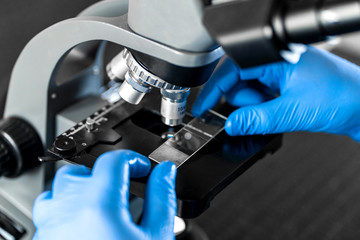 Male laboratory assistant examining biomaterial samples in a microscope. Cllose up hands in blue...