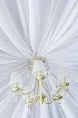 Classic chandelier hanging on ceiling made of white cloth. Bottom view. 