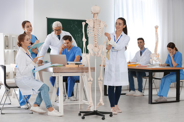 Medical students and professor studying human skeleton anatomy in classroom