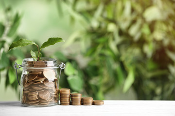 Coins and green sprout on white wooden table against blurred background, space for text. Money savings