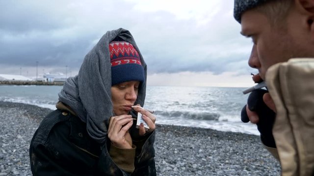 homeless couple, man and woman smoking on the seashore