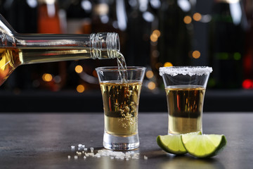 Pouring Mexican Tequila from bottle into shot glass on bar counter © New Africa