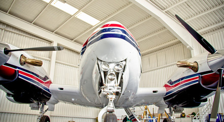 Dramatic low-angle view of a propeller aircraft showcasing shiny fuselage details, photographed from beneath against the clean metallic backdrop of a hangar.