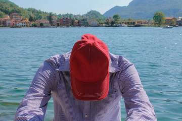 Man in cap relaxing against lake and mountains