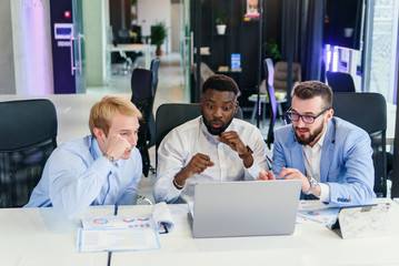 Obraz premium Portrait of handsome amazed satisfied positive bearded young freelancer in blue shirt are sitting in cafe and watching online football match with toothy smile and triumphing. indoor