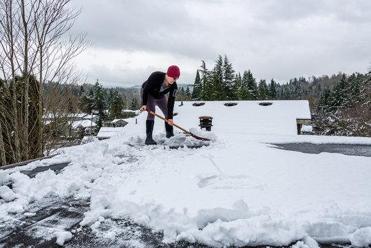 Mature Woman Shoveling Fresh Wet Snow Off A Flat Carport Roof